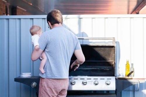 Young dad cooking dinner on the family barbeque in summer - Australian Stock Image