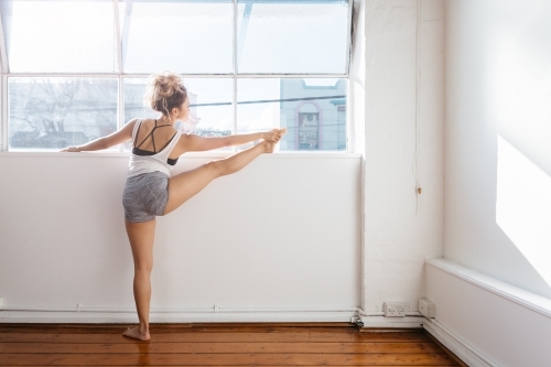 Young dancer touching her toes and stretching on a ledge with sun flare - Australian Stock Image
