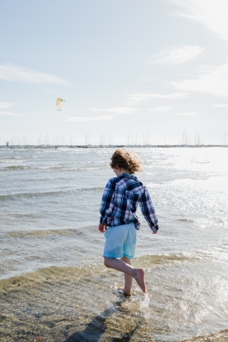 Young dressed boy walking in the ocean at St Kilda Beach, Melbourne, Victoria, Australia - Australian Stock Image