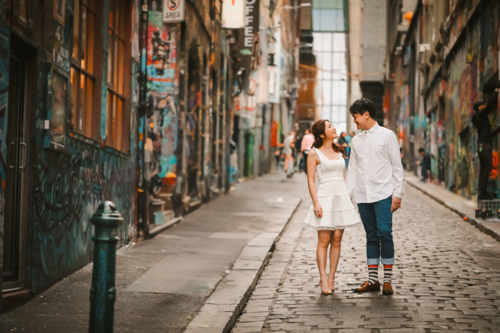 Young engaged couple posing together in Hosier Lane, iconic graffiti laneway in Melbourne city - Australian Stock Image