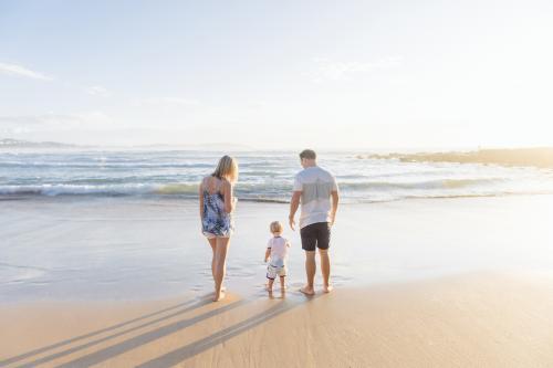 Young family of three standing on the beach at sunrise - Australian Stock Image