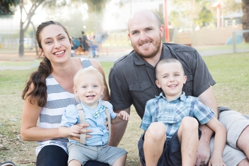 Young family sitting on the park ground smiling - Australian Stock Image