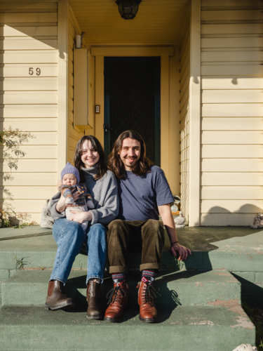 Young family sitting on the steps of their porch on sunny day - Australian Stock Image