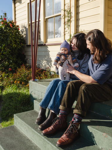 Young family sitting on the steps of their porch on sunny day - Australian Stock Image