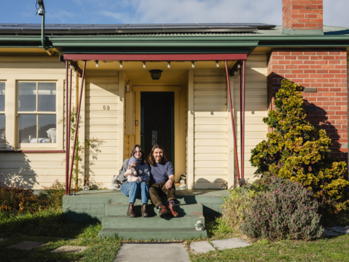 Young family sitting on the steps of their porch on sunny day - Australian Stock Image