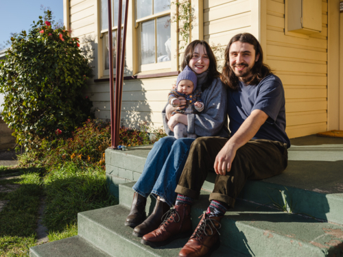 Young family sitting on the steps of their porch on sunny day - Australian Stock Image