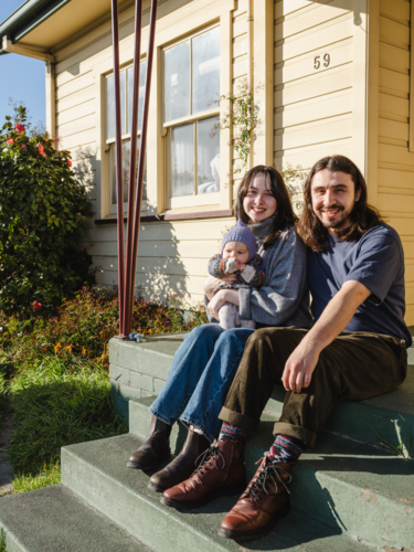 Young family sitting on the steps of their porch on sunny day - Australian Stock Image
