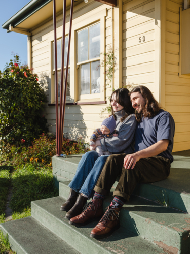 Young family sitting on the steps of their porch on sunny day - Australian Stock Image