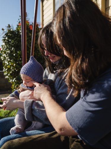 Young family sitting on the steps of their porch on sunny day - Australian Stock Image