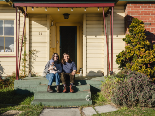 Young family sitting on the steps of their porch on sunny day - Australian Stock Image