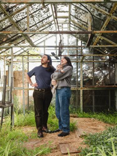Young family standing inside weathered glasshouse - Australian Stock Image