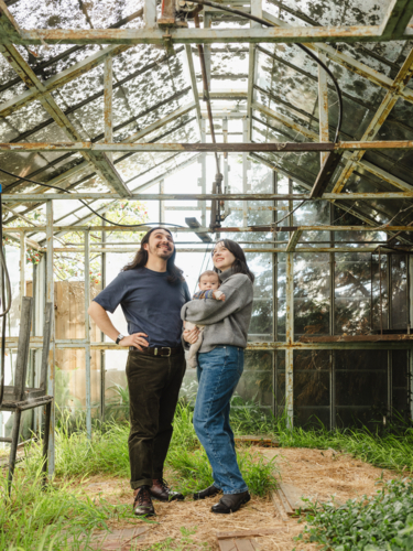 Young family standing inside weathered glasshouse - Australian Stock Image