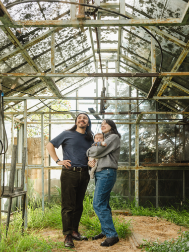 Young family standing inside weathered glasshouse - Australian Stock Image