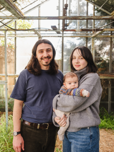 Young family standing inside weathered glasshouse - Australian Stock Image