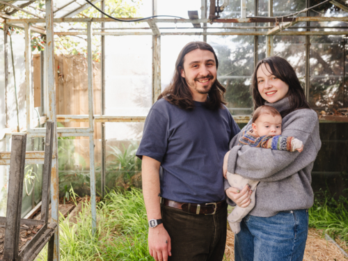 Young family standing inside weathered glasshouse - Australian Stock Image