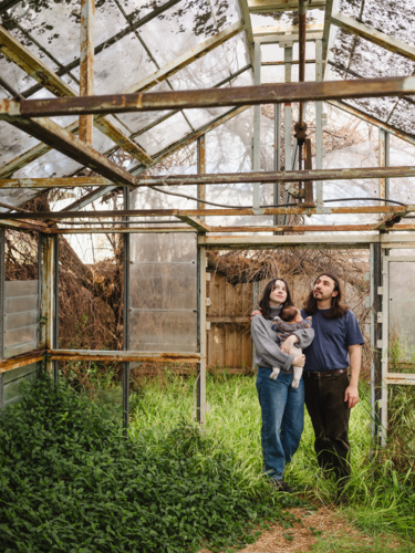 Young family standing inside weathered glasshouse - Australian Stock Image