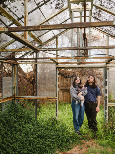 Young family standing inside weathered glasshouse - Australian Stock Image