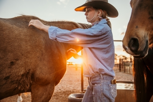 Young farm person patting horse at sunset - Australian Stock Image