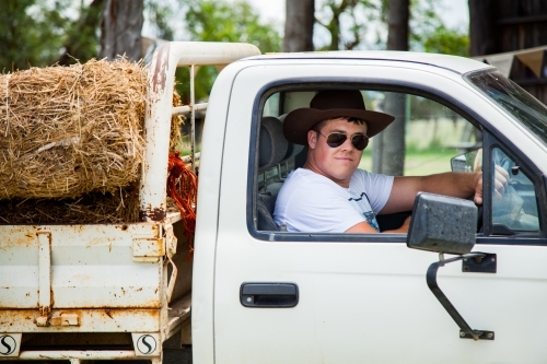 Young farmer in his 20s driving a ute in sunnies and akubra