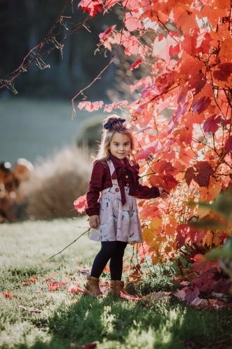 Young fashionable girl standing near autumn leaves smiling - Australian Stock Image