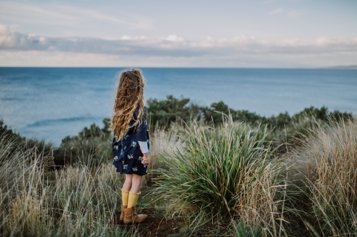 Young fashionable girl standing on a cliff top looking out to the ocean - Australian Stock Image