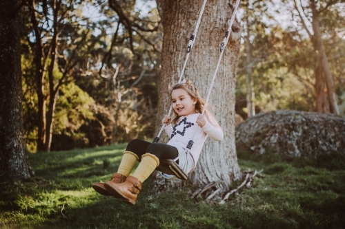 Young fashionable girl swinging on a wooden swing in a farm setting - Australian Stock Image
