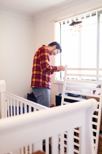 Young father in baby's nursery assembling cot
