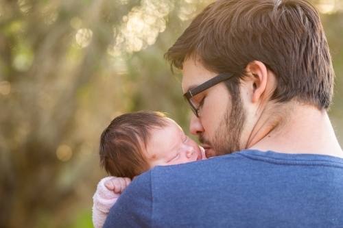 Young father kissing his newborn daughter outside with bokeh copy space - Australian Stock Image