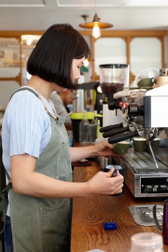 Young female barista preparing coffee with a coffee machine - Australian Stock Image
