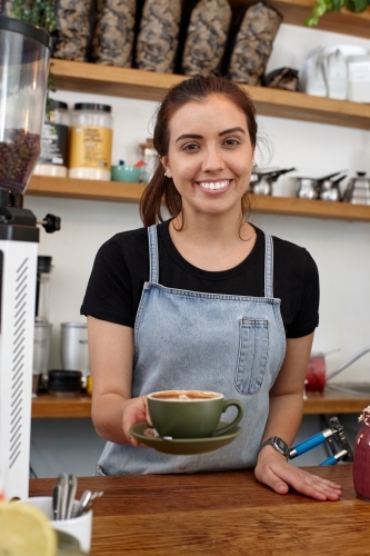 Young female barista serving a fresh hot coffee - Australian Stock Image