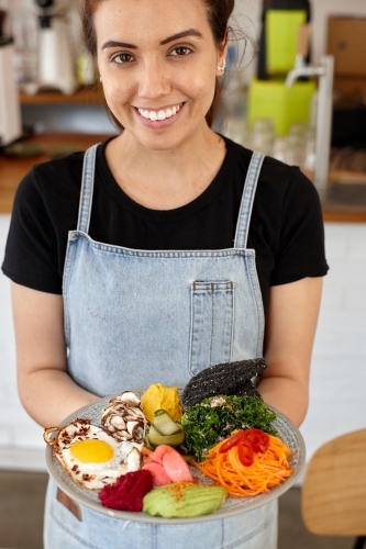 Young female cafe worker holding healthy dish - Australian Stock Image