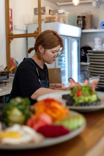 Young female chef in cafe kitchen preparing healthy vegetarian meal - Australian Stock Image