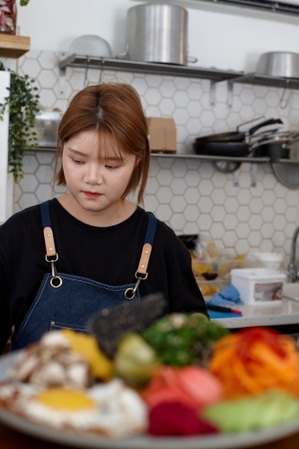 Young female chef in cafe kitchen preparing healthy vegetarian meal - Australian Stock Image