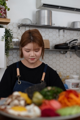 Young female chef in cafe kitchen preparing healthy vegetarian meal