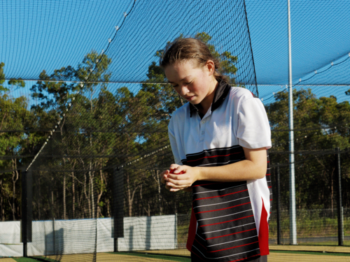Young female cricketer practicing in the nets holding a cricket ball - Australian Stock Image