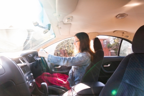 Young female driver driving car with sun flare - Australian Stock Image