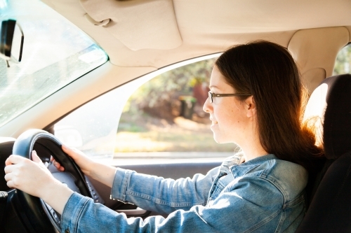 Young female driver driving car with sun flare - Australian Stock Image