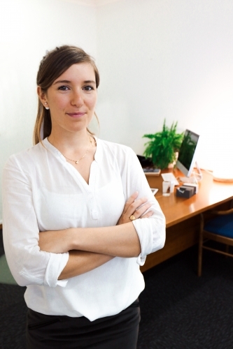 Young female office worker standing with colleague sitting at a computer in the background - Australian Stock Image