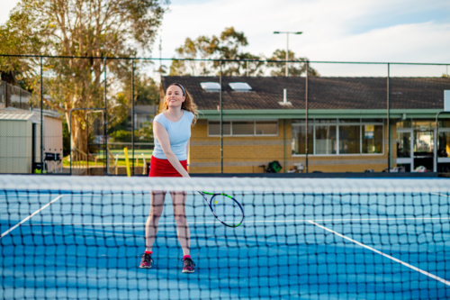Young female tennis player prepares to hit the ball during a tennis match - Australian Stock Image