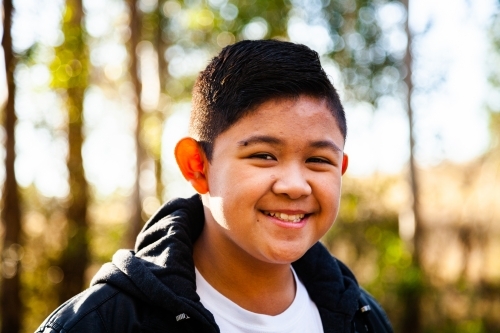 Young Filipino boy in leather jacket smiling in bushland - Australian Stock Image