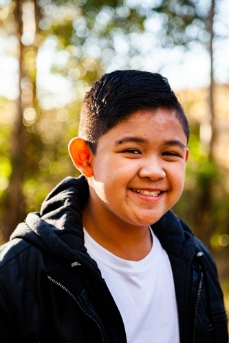Young Filipino boy in leather jacket smiling in bushland - Australian Stock Image