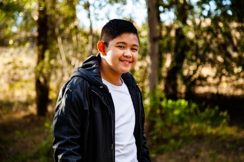Young Filipino boy in leather jacket smiling in bushland - Australian Stock Image