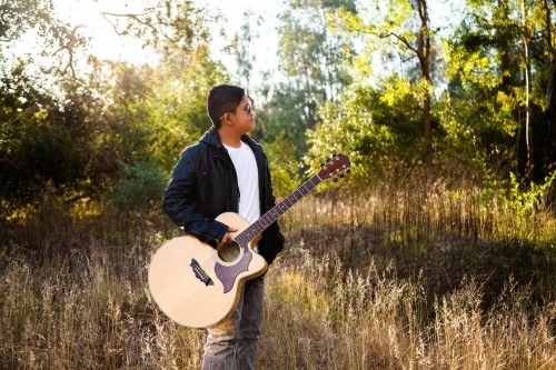 Young Filipino man holding musical instrument outside in nature - Australian Stock Image