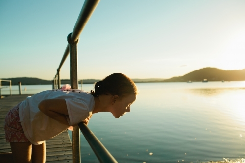 Young girl at a wharf leaning over looking at the water - Australian Stock Image