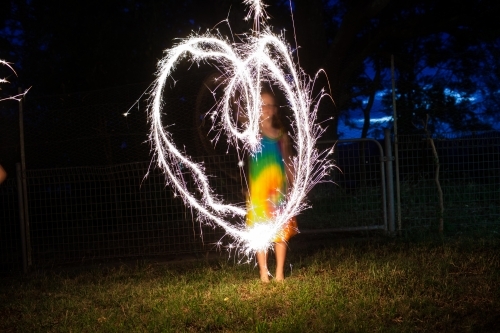 Young girl creating a heart shape with a sparkler at night