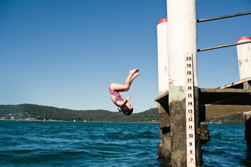 Young girl doing a front flip off a wharf