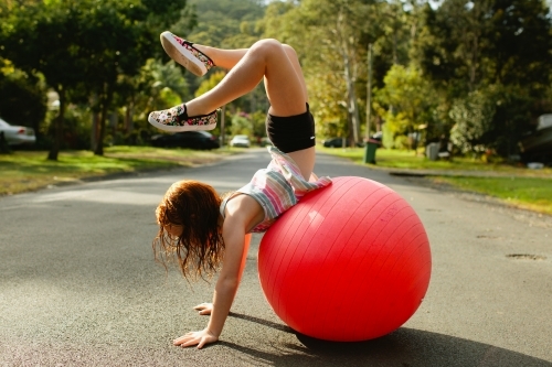 Young girl doing a handstand on an exercise ball on the road - Australian Stock Image