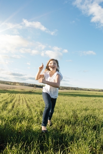 Young girl flying a paper aeroplane in a green farm paddock - Australian Stock Image