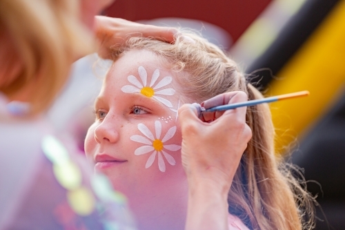 Young girl getting flowers painted on her face at party - Australian Stock Image