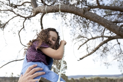 Young girl getting pushed on swing while looking down - Australian Stock Image